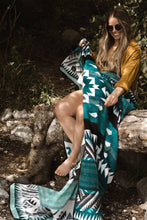 Load image into Gallery viewer, Woman sitting on a log with a green patterned blanket draped over her, surrounded by nature.
