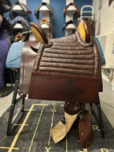 Load image into Gallery viewer, Brown leather saddle on display with a blue blanket underneath, against a background of other saddles.
