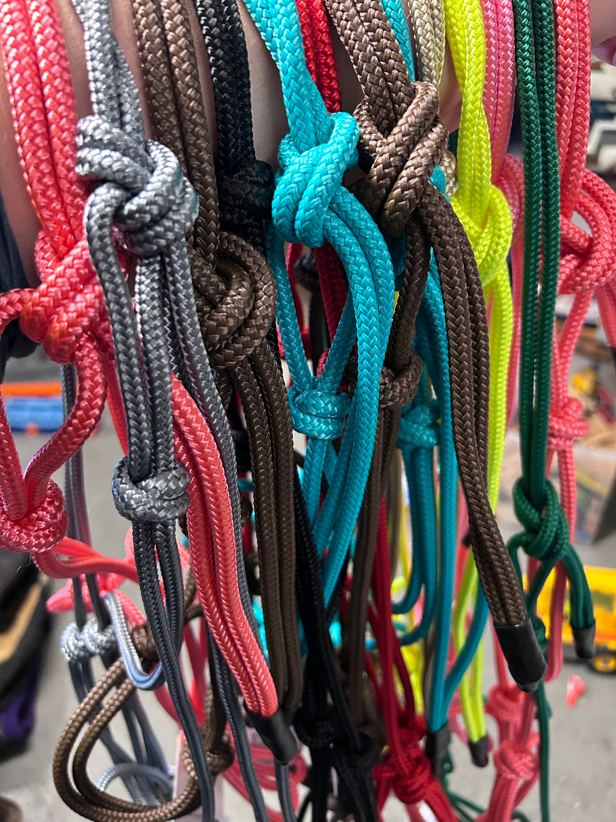 A close-up of multiple braided rope cords in different colors hanging vertically, including red, gray, black, turquoise, brown, neon yellow, and green, with knots and loop ends visible.