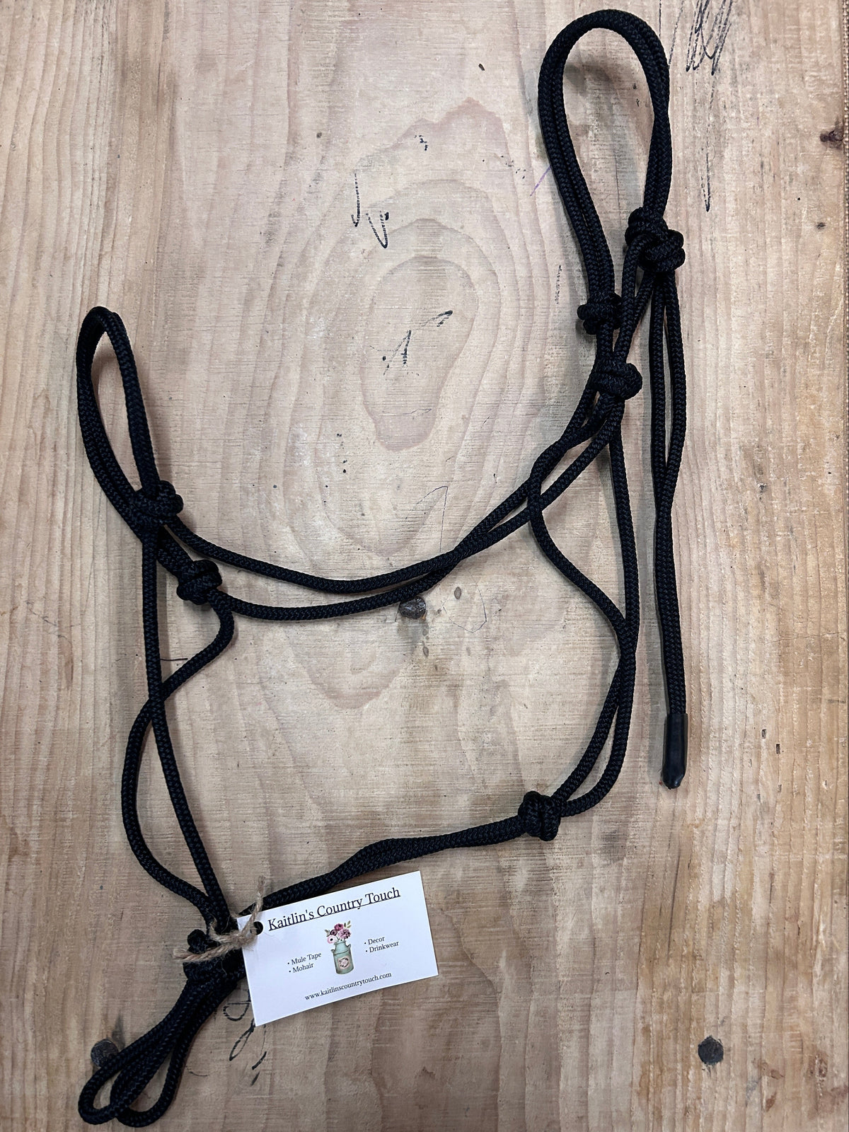 Black braided rope halter with a white product tag, displayed on a light-colored wooden surface.