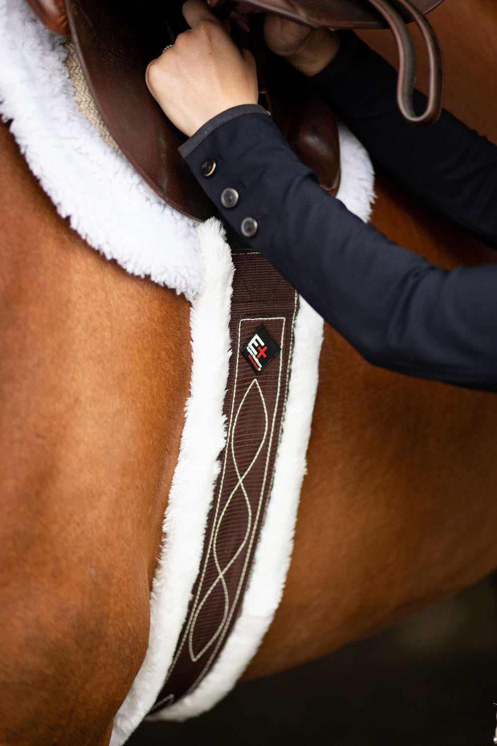 Person adjusting a brown saddle pad on a horse