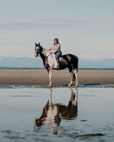 Girl on a black and white horse bareback on a beach with their reflection