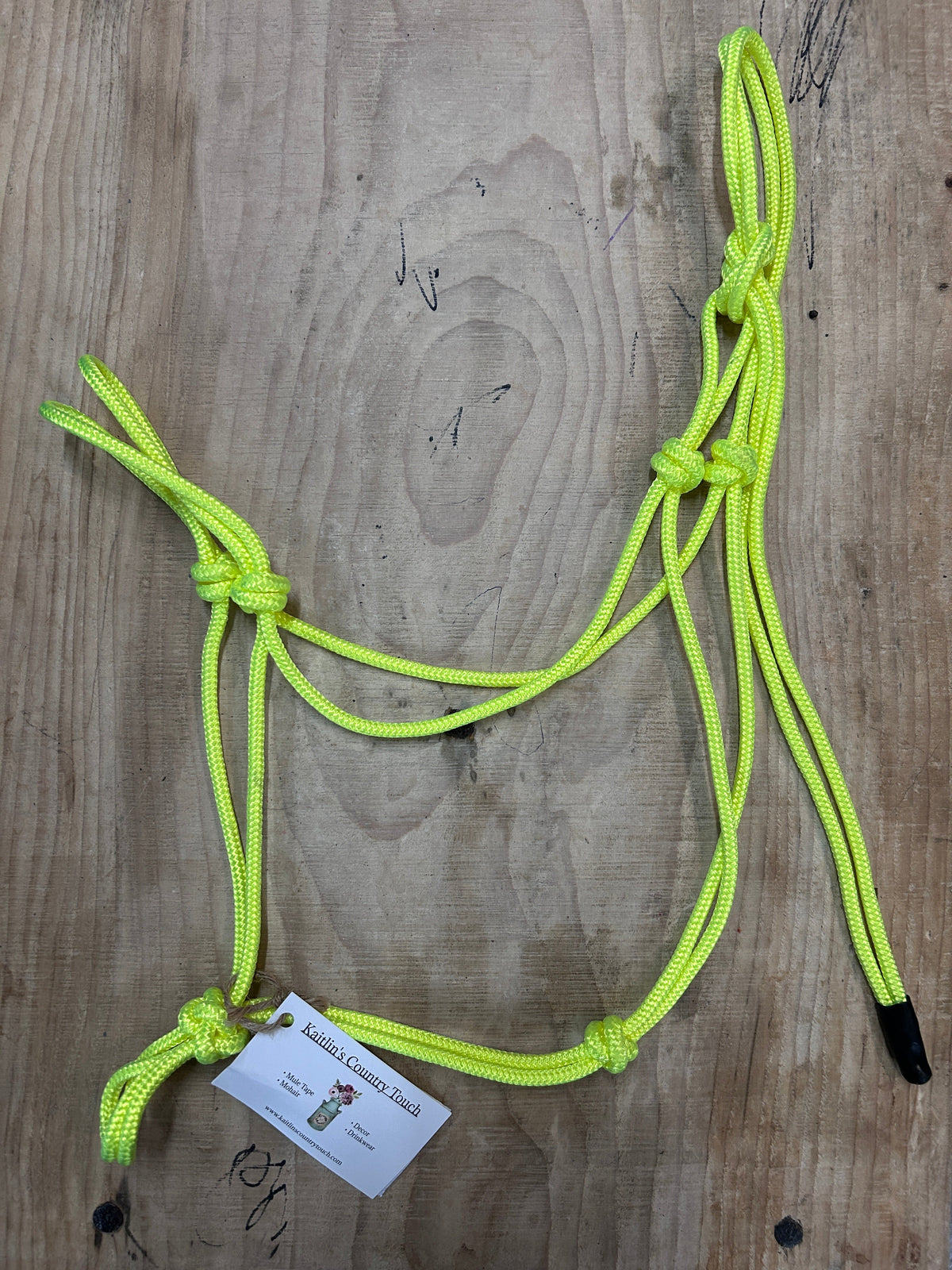 A neon yellow-green braided rope laid out on a wooden surface, with black end caps, several knots, and a small white product tag attached near one end.
