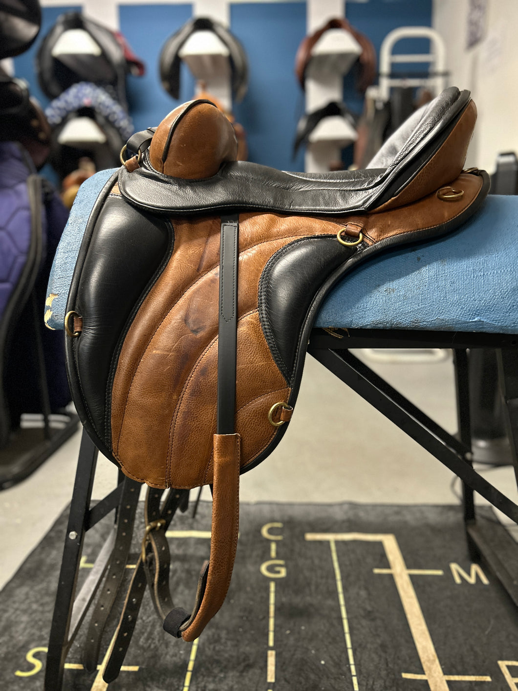 Brown leather saddle on a blue seat with a blurred background of horse saddles.