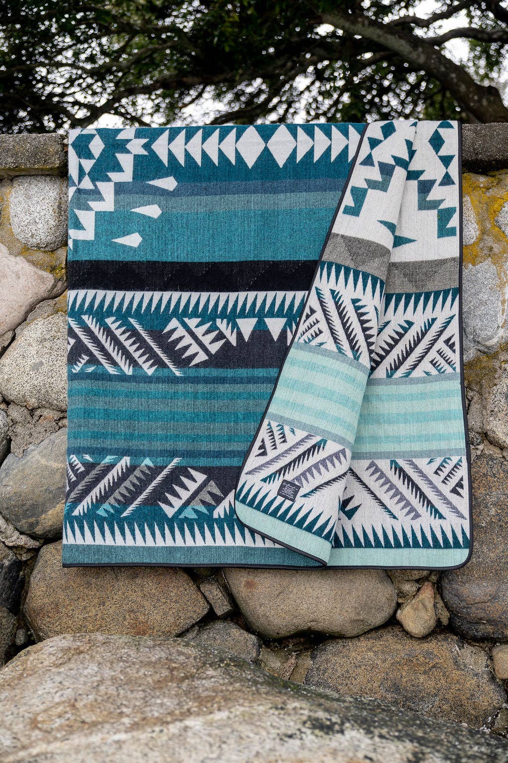 Two patterned blanket draped over a stone wall with a natural background.