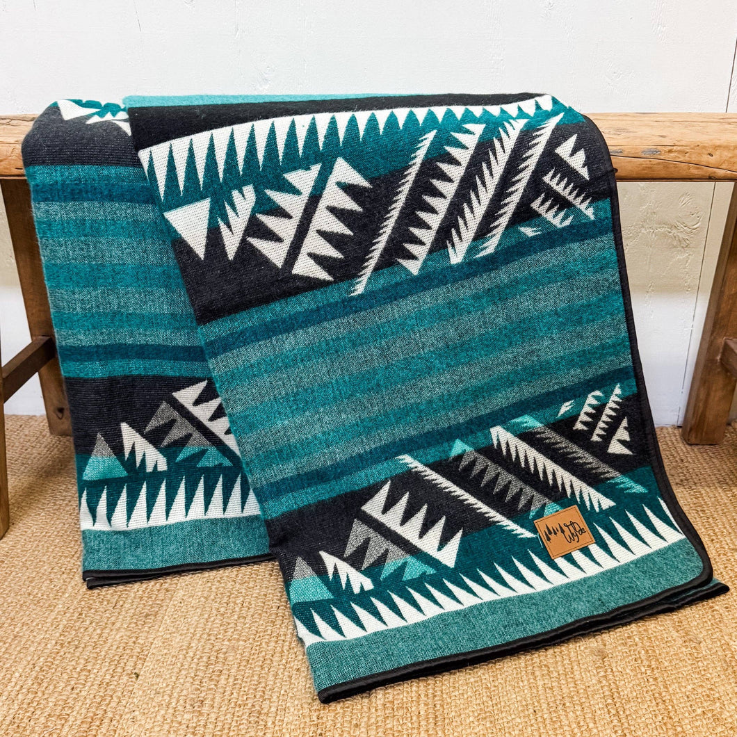 Teal and black patterned blanket with white geometric designs on a wooden surface.