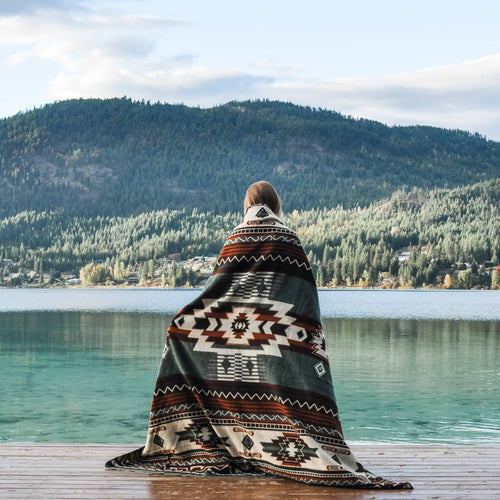 Person wrapped in a patterned blanket overlooking a lake and mountains